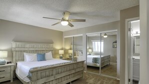 A bedroom with a wooden bed, bedside lamps, a ceiling fan, and a large mirror.