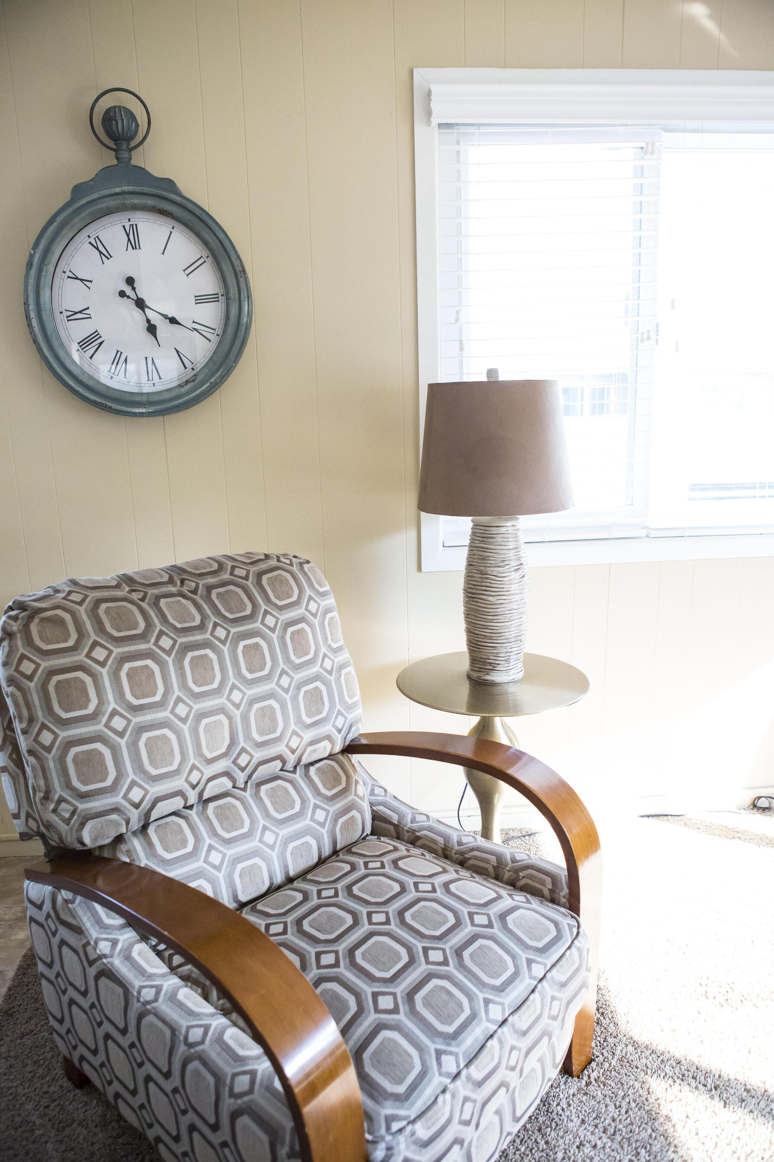 A chair with a geometric pattern, a round table with a lamp, and a wall clock.