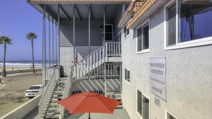Un edificio frente a la playa con balcón, escalera y un anuncio de alquileres vacacionales.