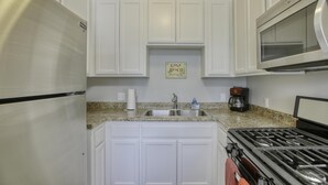 Una cocina con armarios blancos, un refrigerador de acero inoxidable, microondas, estufa a gas y encimera de granito.