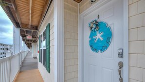 Un passadís amb una porta blanca, persianes verdes i un cartell blau de benvinguda amb una estrella.