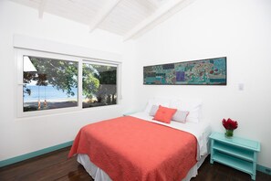 A bedroom with a bed, a window with a view of the beach, and a painting on the wall. - Beachfront Oasis in Playa Hermosa, Guanacaste (Playa Hermosa)