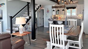 A modern kitchen with a central island, pendant lighting, and a staircase leading to an upper level. - Experience oceanfront bliss at Summer Wind West in Oak Island! Ideal for 12 guests. (Oak Island)