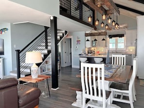 A modern kitchen with a central island, pendant lighting, and a staircase leading to an upper level.