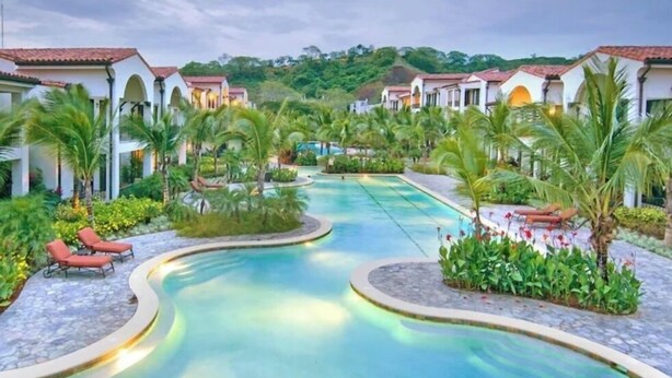 A resort with a swimming pool, palm trees, and a hilly backdrop. - Stunning Ocean View from Luxury Two Bedroom in Pacifico  - Perfect Coco Location (Playa del Coco)