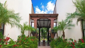 A pathway leading to a covered entrance with a tiled floor, surrounded by lush greenery and red flowers. - Stunning Ocean View from Luxury Two Bedroom in Pacifico  - Perfect Coco Location (Playa del Coco)