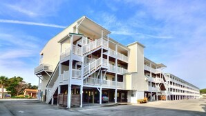 A multi-story hotel with balconies, a central staircase, and a parking area. - Oceanview retreat in Oak Island, 3BR condo with pool access and family amenities. (Oak Island)