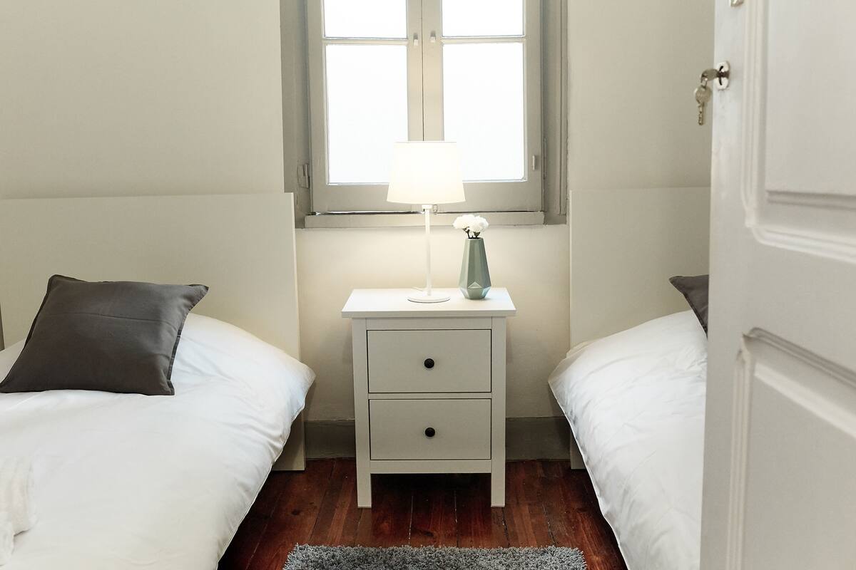 Une chambre avec deux lits, une table de chevet avec une lampe et une fenêtre.