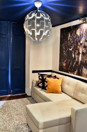Een moderne woonkamer met een witte bank, een lamp in de vorm van een wereldbol, een poster met een stadsgezicht en een blauwe deur.