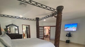 Um quarto espaçoso com uma cama de dossel, televisão fixada na parede e uma janela grande.