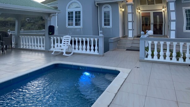 Um imóvel residencial com piscina, alpendre coberto e entrada bem iluminada.