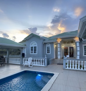 A residential property with a swimming pool, a covered patio, and a well-lit entrance.