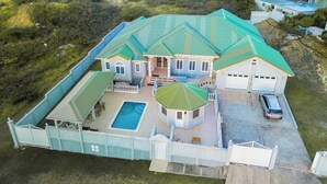 Uma casa grande com piscina, várias garagens e um quintal cercado.