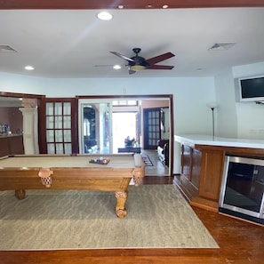 A spacious living area with a pool table, a ceiling fan, and a kitchen area with a microwave.