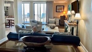 A modern living room with a large sofa, a coffee table, and a dining area with a table and chairs. - Oceanfront 3br/3ba Shipwatch Villa, Oceanfront (Fernandina Beach)