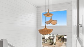 A room with white paneled walls, a window with a view of a street, and two hanging wicker lamps. - Experience oceanfront luxury at Pier Magic, Oak Island – 6 bedrooms for up to 16 guests. (Oak Island)