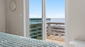 A bedroom with a bed, a sliding glass door leading to a balcony with a view of the sea and a pier. - Experience oceanfront luxury at Pier Magic, Oak Island – 6 bedrooms for up to 16 guests. (Oak Island)