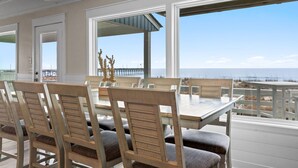 A dining area with a view of the beach, wooden chairs, and a table. - Experience oceanfront luxury at Pier Magic, Oak Island – 6 bedrooms for up to 16 guests. (Oak Island)