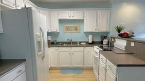 A kitchen with white cabinets, a refrigerator, a sink, and a countertop with a plant and utensils. - Escape to OW 7102-A Sweet Retreat, a 3-bedroom oceanview condo in beautiful Oak Island. (Oak Island)
