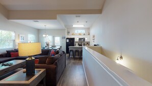 Een moderne keuken met een centraal eiland, een eethoek met een bank en een lamp, en uitzicht buiten door grote ramen.