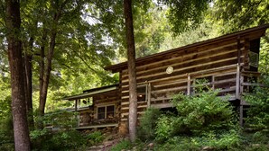 Una cabana de fusta rústica amb un porxo, envoltada per un bosc dens.