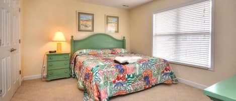 A bedroom with a bed, a nightstand, a lamp, a ceiling fan, and a window with blinds.