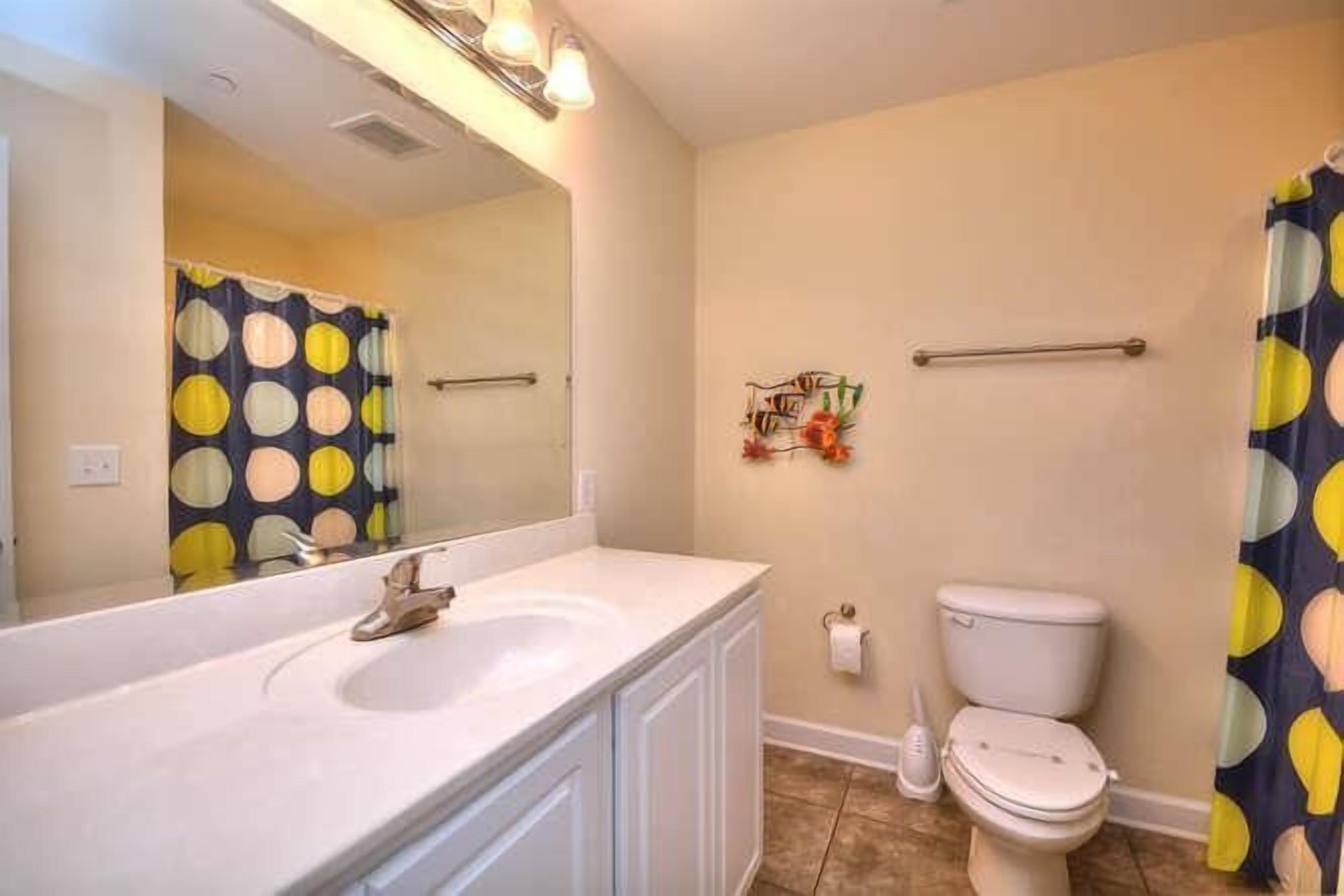Un baño con lavamanos blanco, inodoro y cortina de ducha con estampado de lunares.