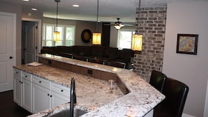 A kitchen with a granite countertop, white cabinetry, and a built-in island with a sink. There are pendant lights above the island and a brick accent wall. - Have it All!!! True Water Front, Amazing Views (Golden)