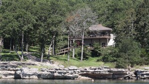 A lakeside cabin with a deck and stairs leading to a balcony, surrounded by dense trees. - Have it All!!! True Water Front, Amazing Views (Golden)