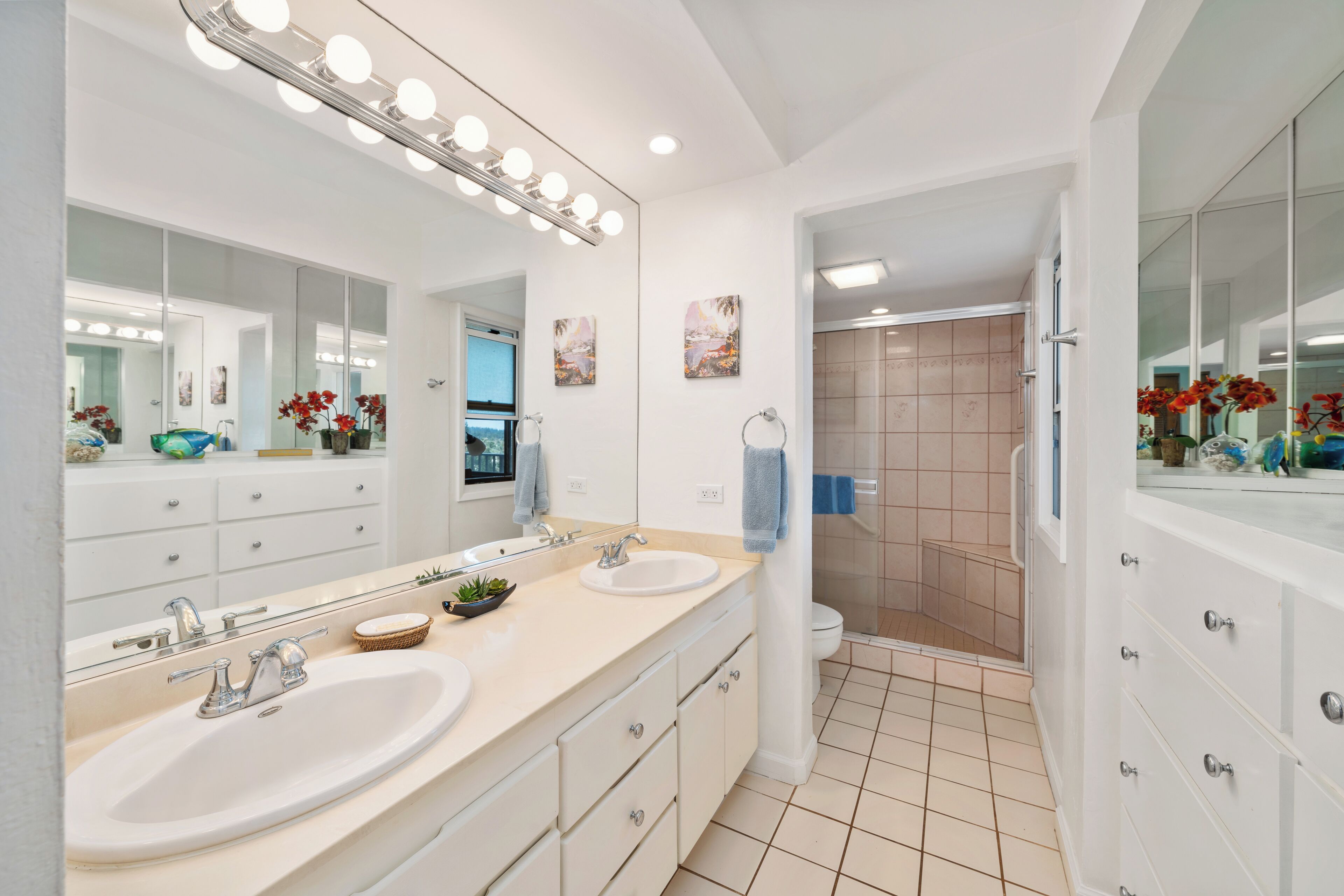 A modern bathroom with two sinks, a large mirror with lights, and a shower area.