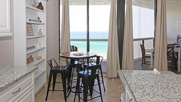 A room with a dining table and chairs, a bookshelf, and a view of the ocean. - Sunshine Daydream-Panoramic Gulf Views from Every Room! Beach Chair Svc Included (Miramar Beach)