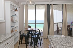 A room with a dining table and chairs, a bookshelf, and a view of the ocean. - Sunshine Daydream-Panoramic Gulf Views from Every Room! Beach Chair Svc Included (Miramar Beach)