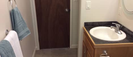 Un baño con tocador de madera, un lavamanos blanco y un perchero para toallas.