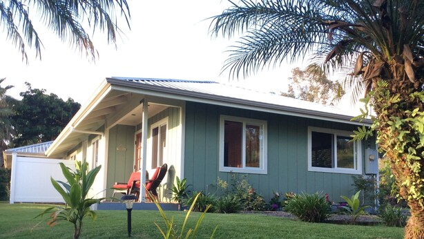 A single-story house with a porch, a covered outdoor seating area, and a well-maintained lawn.