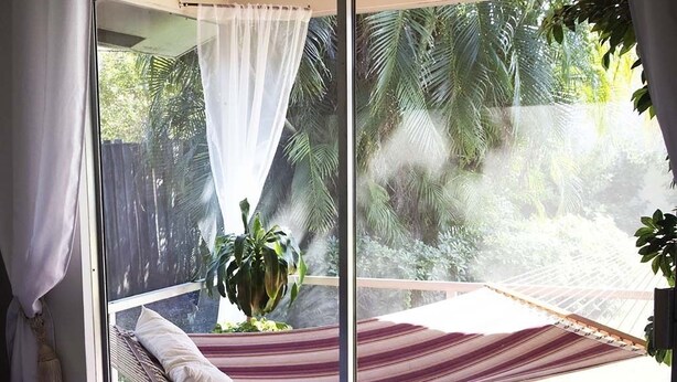 A hammock bed with a view of tropical foliage through a glass door.