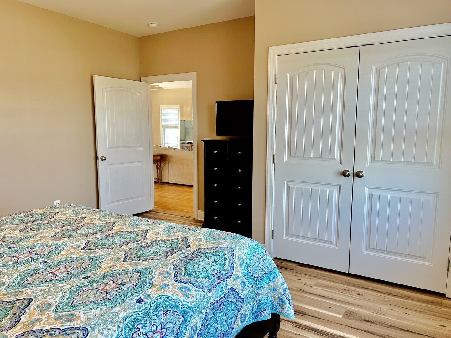 A bedroom with a bed, a dresser, and a TV. There are two doors, one open and one closed.