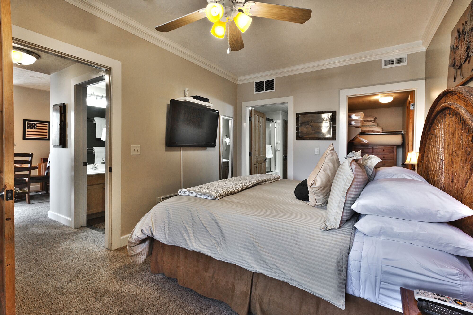 A bedroom with a bed, a ceiling fan, a television, and a wooden headboard.