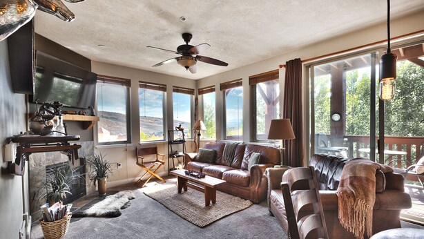 A spacious living room with a large window, a ceiling fan, and a fireplace.