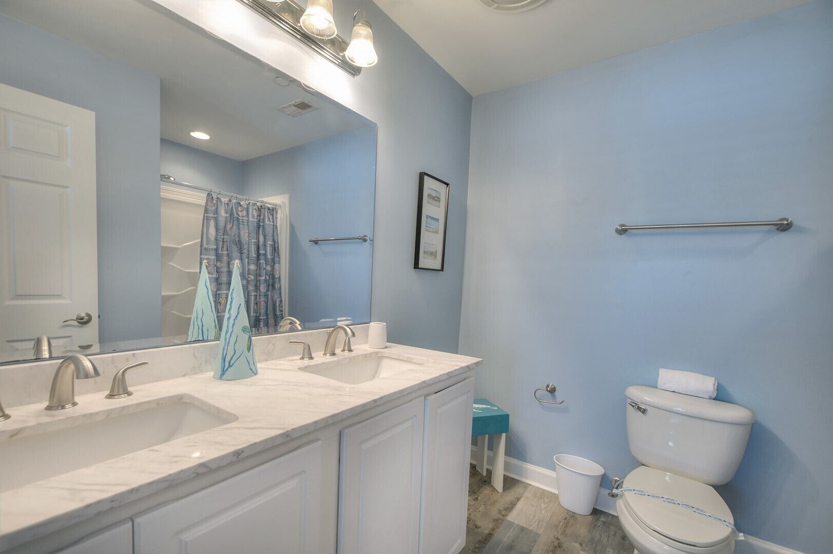 Une salle de bain avec un meuble-lavabo à deux vasques, des toilettes, une douche avec un rideau et un porte-serviettes.