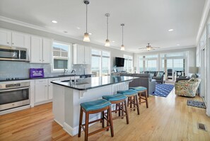 A modern kitchen with a central island, bar stools, and a dining area with a view.