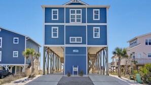 A multi-story building with a central entrance, a sign indicating a beach location, and a wooden deck structure. - Discover oceanfront bliss at 7th Heaven in Oak Island, NC—spacious 7BR, sleeps 24! (Oak Island)