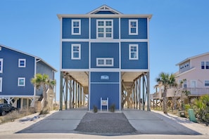 Un immeuble à plusieurs étages doté d’une entrée centrale, d’une enseigne indiquant qu’il est situé près d’une plage, et d’une structure de terrasse en bois.