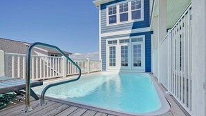 A swimming pool with a wooden deck, a white fence, and a building with blue siding and white trim. - Discover oceanfront bliss at 7th Heaven in Oak Island, NC—spacious 7BR, sleeps 24! (Oak Island)