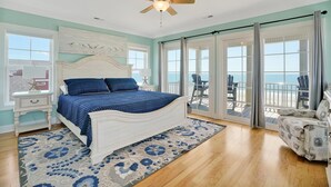 A bedroom with a bed, a nightstand, a desk, a chair, a ceiling fan, and a view of the ocean through large glass doors. - Discover oceanfront bliss at 7th Heaven in Oak Island, NC—spacious 7BR, sleeps 24! (Oak Island)
