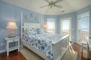 Une chambre à coucher avec un lit, des tables de chevet, un ventilateur de plafond et une vue sur l’extérieur.