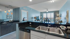 A modern kitchen with a double sink, a dishwasher, and a view to the living area.