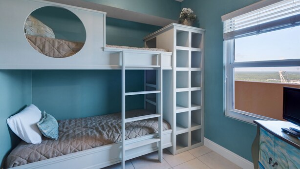 A bunk bed with a circular window, a small desk, and a window with a view of a landscape.