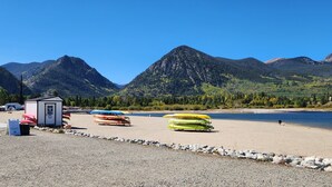 A lakeside beach with kayaks, a small cabin, and mountains in the background.