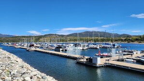 A marina with boats docked along a rocky shoreline, surrounded by mountains and clear skies.