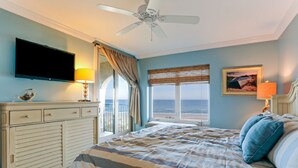 A bedroom with a bed, a TV, a ceiling fan, a window with a view, and a nightstand with a lamp. - Beautiful 2br/2ba Oceanfront, Sea Dunes  (Amelia Island)